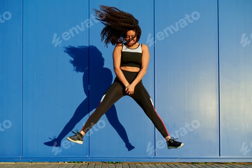 Preview: Young sporty woman jumping with blue wall background