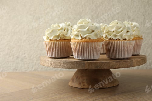 Preview: Tasty vanilla cupcakes with cream on wooden table