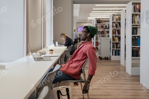 Preview: Unhappy black guy student feeling overwhelmed with study while studying online in library