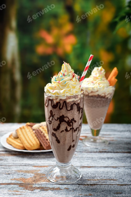 Preview: Chocolate milkshake with whipped cream decorated with sprinkles on a wooden table.