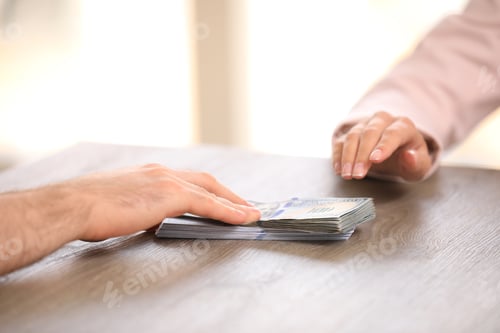 Preview: Man giving dollar bills to businesswoman at wooden table, closeup