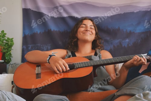Vista previa: Young girl or woman is sitting with eyes closed smiling while playing guitar