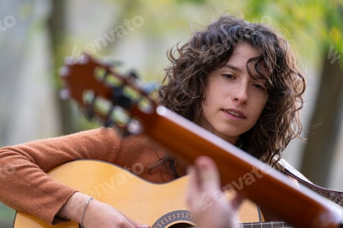 Preview: Young woman learning to play acoustic guitar in the park with a teacher