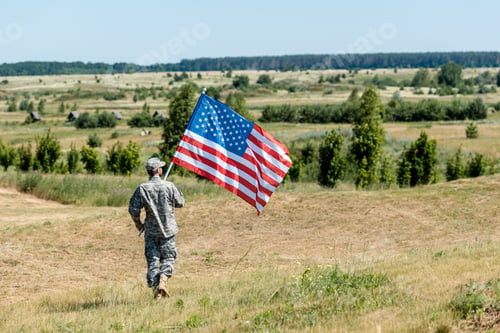 Preview: soldier in uniform walking on grass and holding american flag