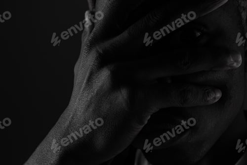 Preview: Close-up portrait of a dark-skinned guy with eyes closed by hand in black and white light