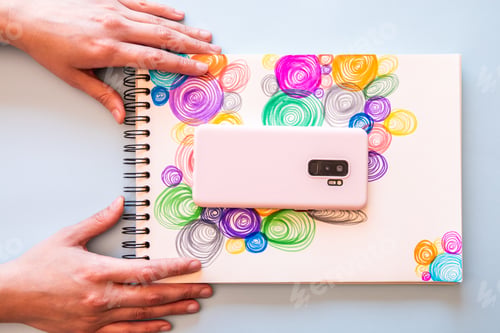Preview: Top view of a person putting a notepad with colorful circles and a phone on it on the table