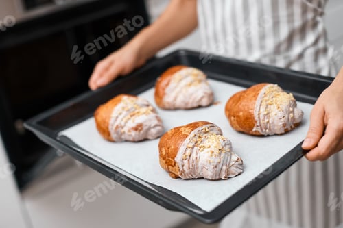 Preview: Baker holding metal tray with freshly baked crispy golden croissants