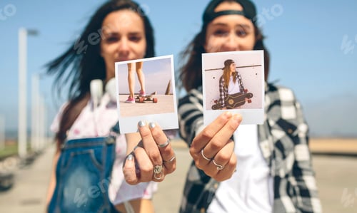 Preview: Two young women showing instant photos with their longboards