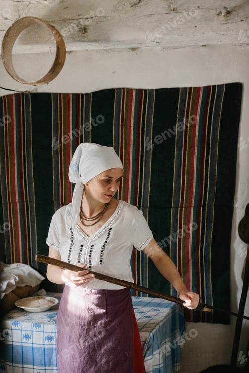 Preview: A woman in Ukrainian national dress works near a wood-burning stove.