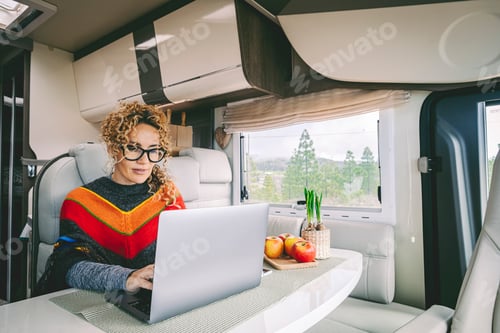 Preview: Independent woman sitting inside a camper van in smart remote working job activity using laptop