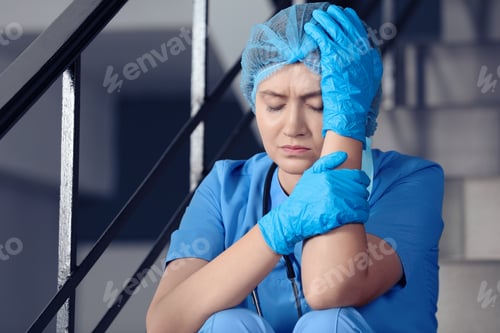 Preview: Exhausted doctor sitting on stairs in hospital