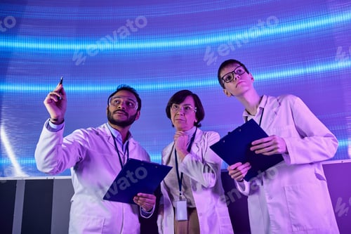 Preview: future-oriented, indian scientist pointing with pen near team in innovative science center