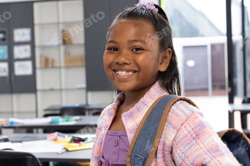 Preview: girl child standing and smiling in elementary school classroom, with denim backpack strap