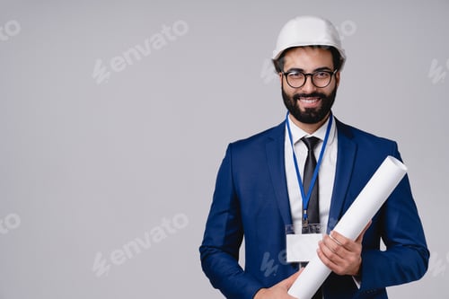 Preview: Cheerful young Arabian engineer with architectural plan and hardhat isolated over grey background