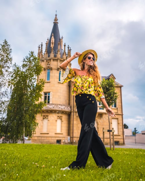 Preview: Blonde woman in a yellow vintage outfit with a hat walking next to a castle