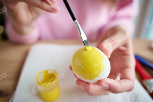 Vista previa: Woman painting Easter egg with yellow paint at table
