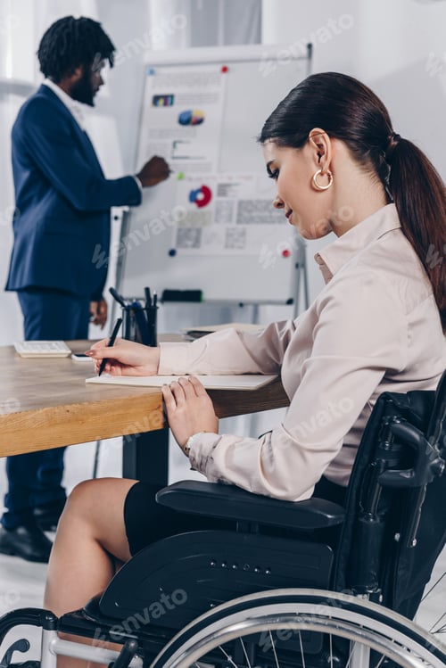 Preview: African american recruiter near flip chart and disabled employee writing in notebook
