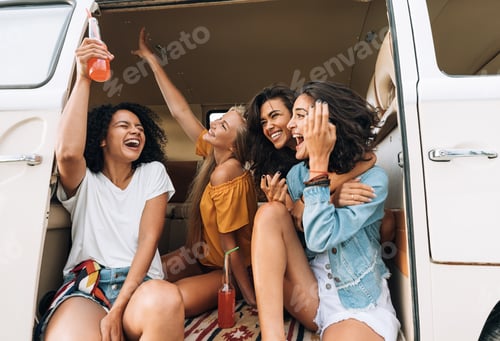 Preview: Multi ethnic group of women hanging out during road trip. Friends in van raising hands and laughing.