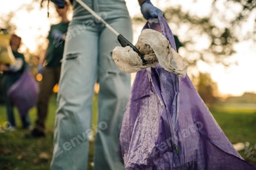 Preview: Volunteer picking up trash with trash grabber tool in public park