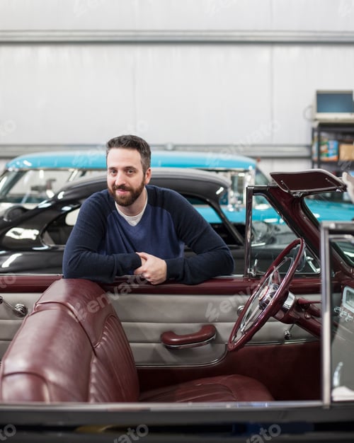 Preview: A portrait of a caucasian male leaving on the side of his classic car convertible in a repair shop.