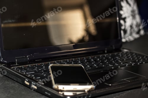 Preview: Closeup shot of a golden smartphone lying on top of the black laptop