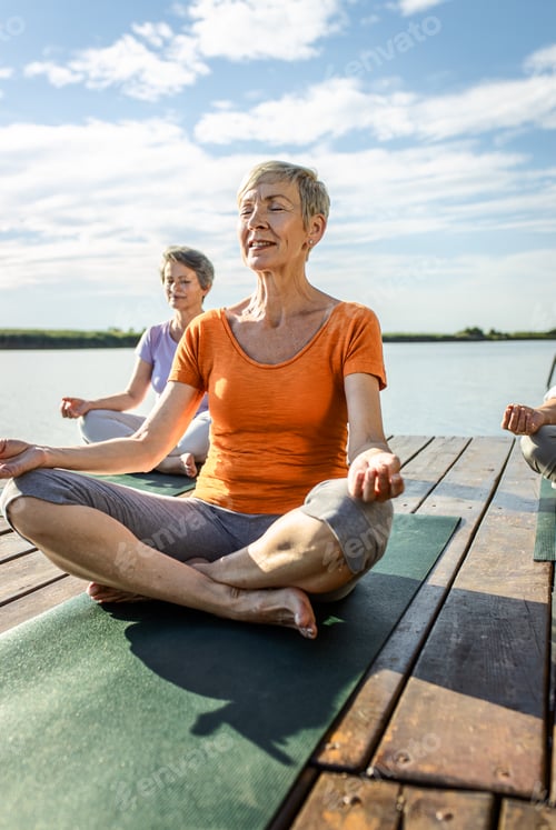 Preview: Group of senior woman doing yoga exercises by the lake.