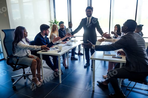 Preview: creative team of multiracial men sitting round the desk in formal clothes talking over
