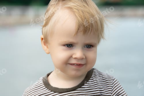 Preview: Blond child smiles face portrait on blurry blue sea background