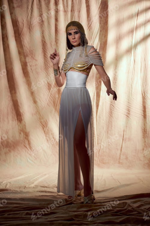 Preview: Trendy model in egyptian attire and pearl top posing while standing on abstract background