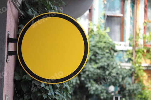 Preview: Yellow circular sign hanging near urban greenery
