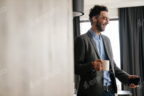 Preview: Handsome laughing guy using mobile phone while drinking coffee