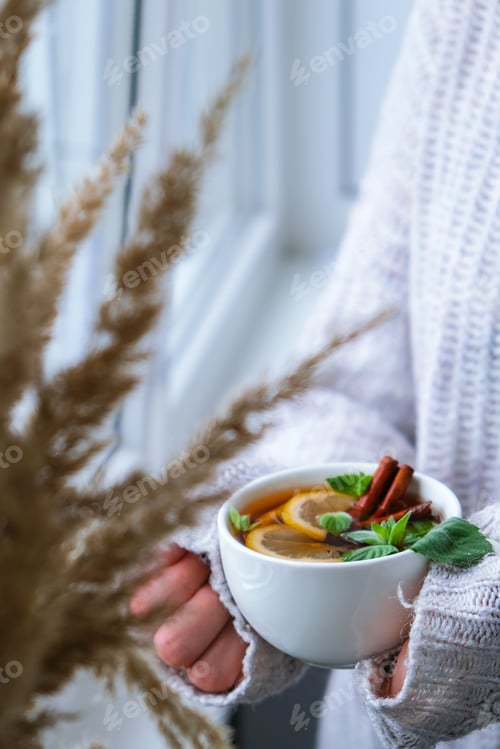 Preview: Woman Holds Cup of Tea with Lemon and Cinnamon