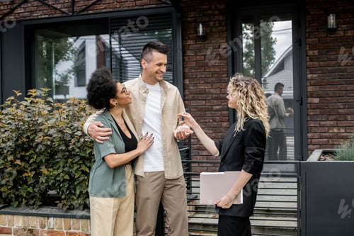 Preview: successful property agent giving key to happy multiethnic couple near house on city street
