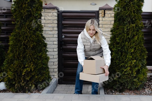 Preview: Woman picking up delivered cardboard boxes in front of her house