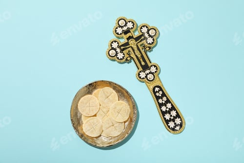 Preview: Golden cross and liturgical bread on golden plate on blue background, top view