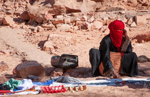 Preview: Bedouin woman with covered face sits on sand in desert