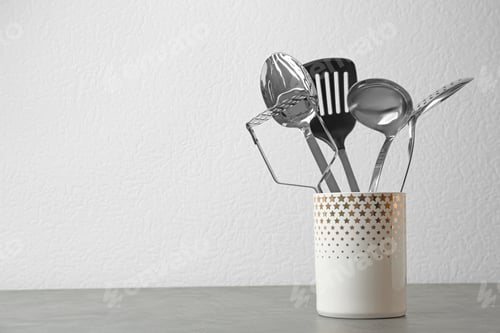 Preview: Set of kitchen utensils in stand on stone table near light wall. Space for text