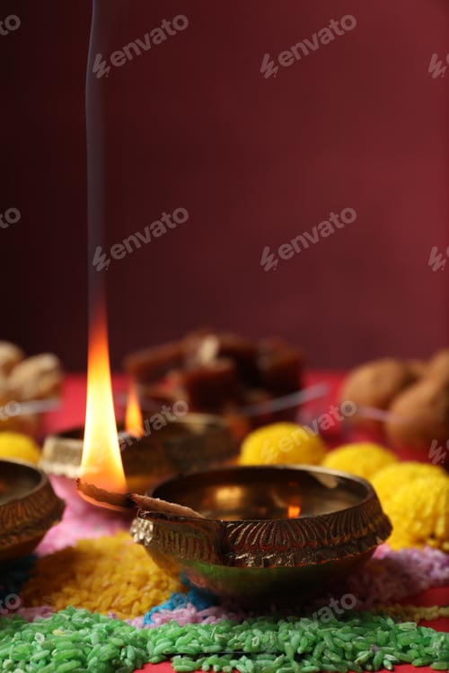 Preview: Diwali celebration. Diya lamps and colorful rangoli on red table, closeup. Space for text