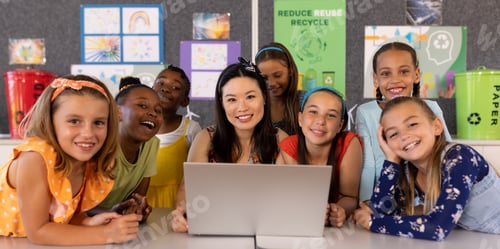 Preview: Portrait of smiling diverse female teacher and schoolgirls with laptop on desk in classroom