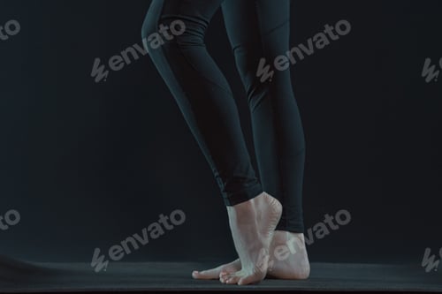 Preview: Young woman legs practicing yoga on yoga mat on a dark black background. copy space