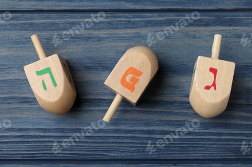 Preview: Hanukkah traditional dreidels with letters He, Pe and Gimel on blue wooden table, flat lay