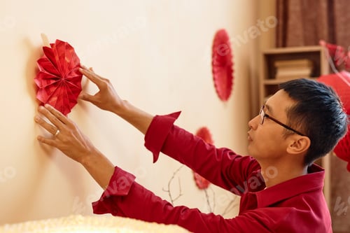 Preview: Asian man hanging red paper decorations on wall for Chinese New Year celebration