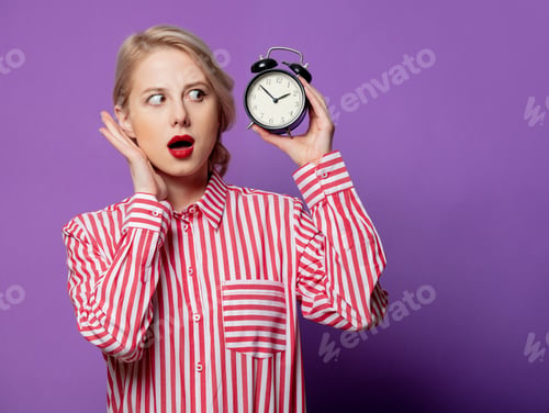 Preview: Beautiful woman in red striped shirt with alarm clock on purple background