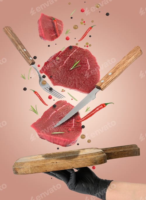 Preview: Raw pieces of beef, rosemary, spices and red chili peppers fall on a wooden cutting board
