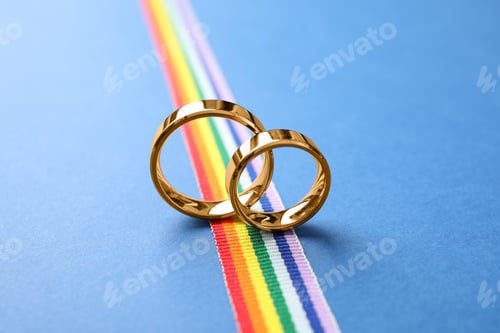 Preview: Wedding rings and rainbow ribbon on color background. Gay symbol