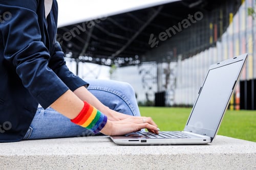 Preview: Close-up of woman hands with laptop and LGBT bracelet in modern park . LGBTQIA culture.