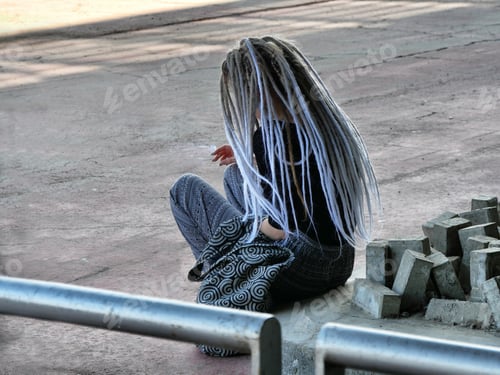 Preview: Closeup shot of a female with dreadlocks sitting on concrete