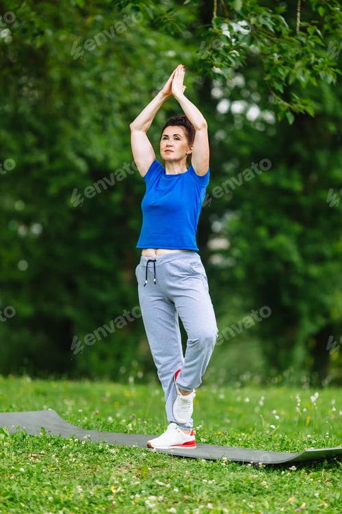 Preview: Aged female doing yoga exercise in park. Senior woman practicing yoga outdor