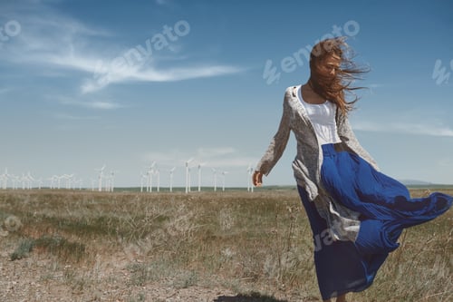Preview: Woman with long tousled hair next to the wind turbine with the wind blowing