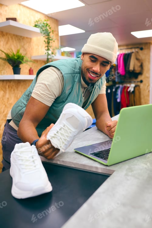 Preview: Male Sales Assistant At Cash Desk In Pop Up Fashion Or Clothes Store Selling Pair Of Trainers